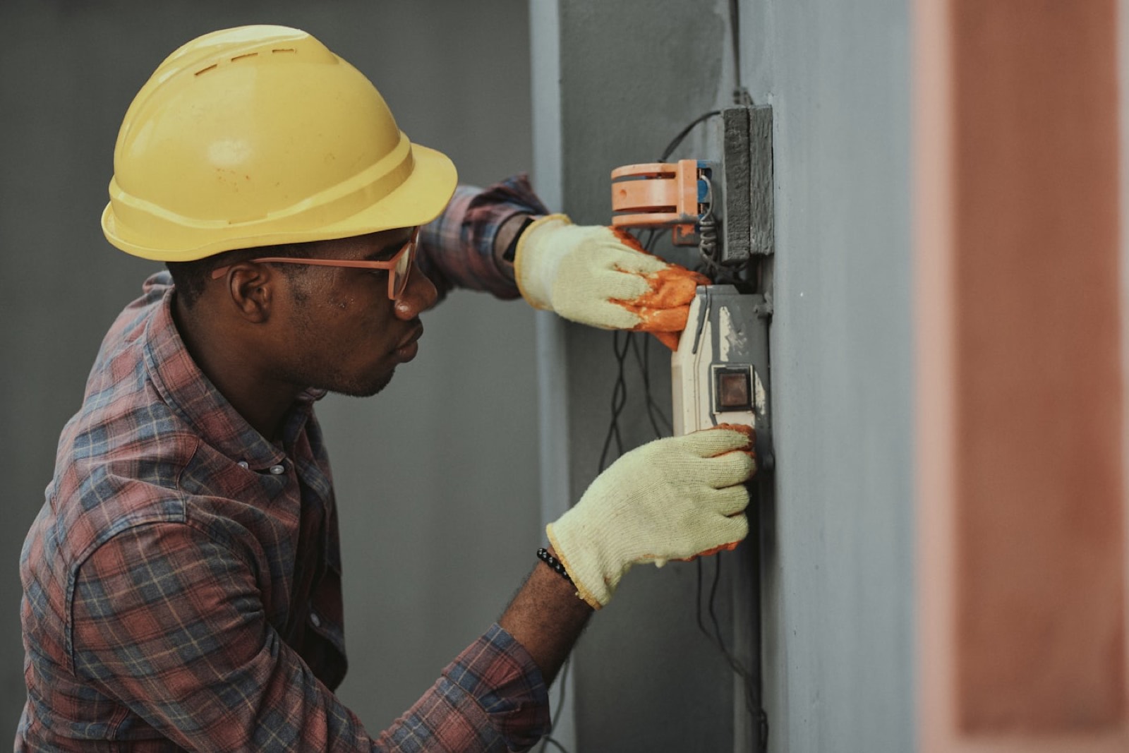 An electrician in a hard hat wiring a junction box.